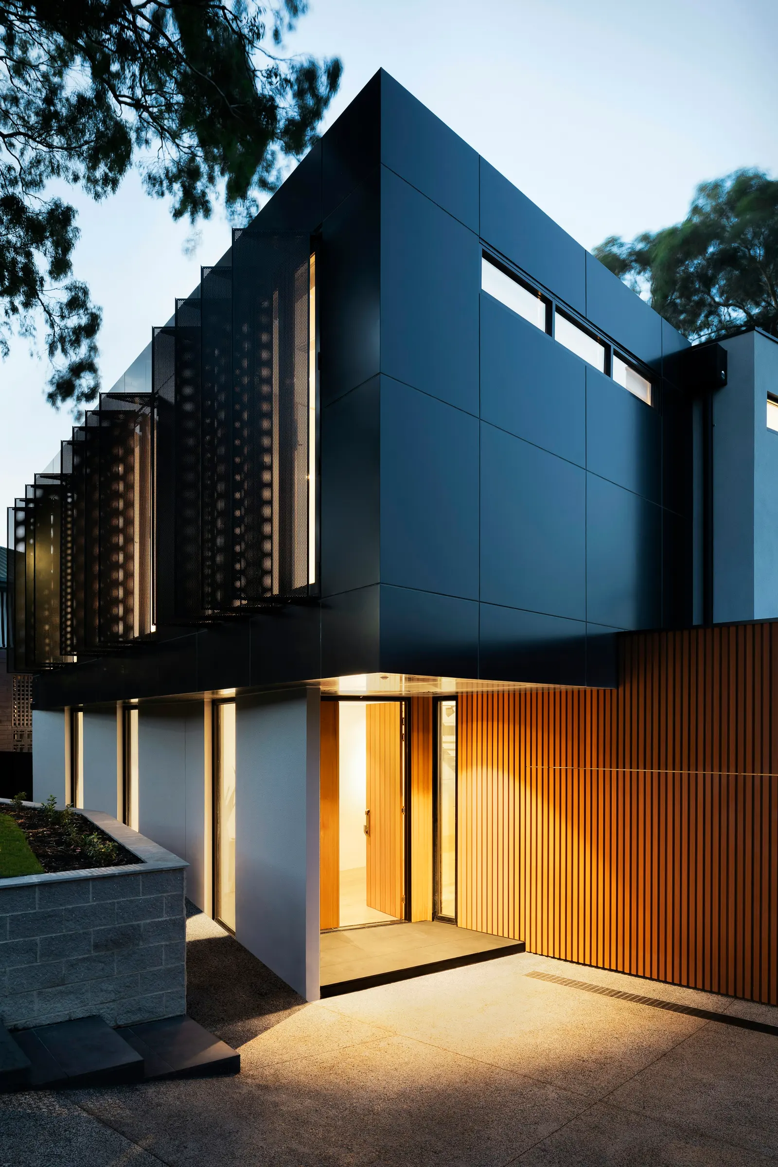 Contemporary black-clad house with a warmly lit entrance and timber cladding at dusk