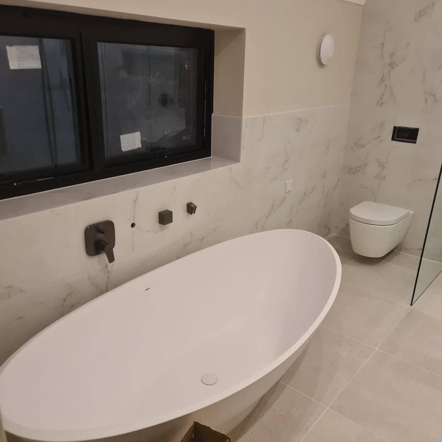Freestanding stone bath beneath a window, with wall-mounted black taps