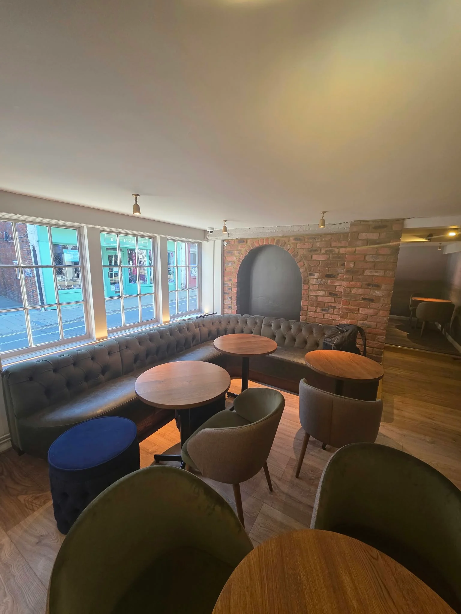 Lounge area with a buttoned banquette, round tables and exposed brick