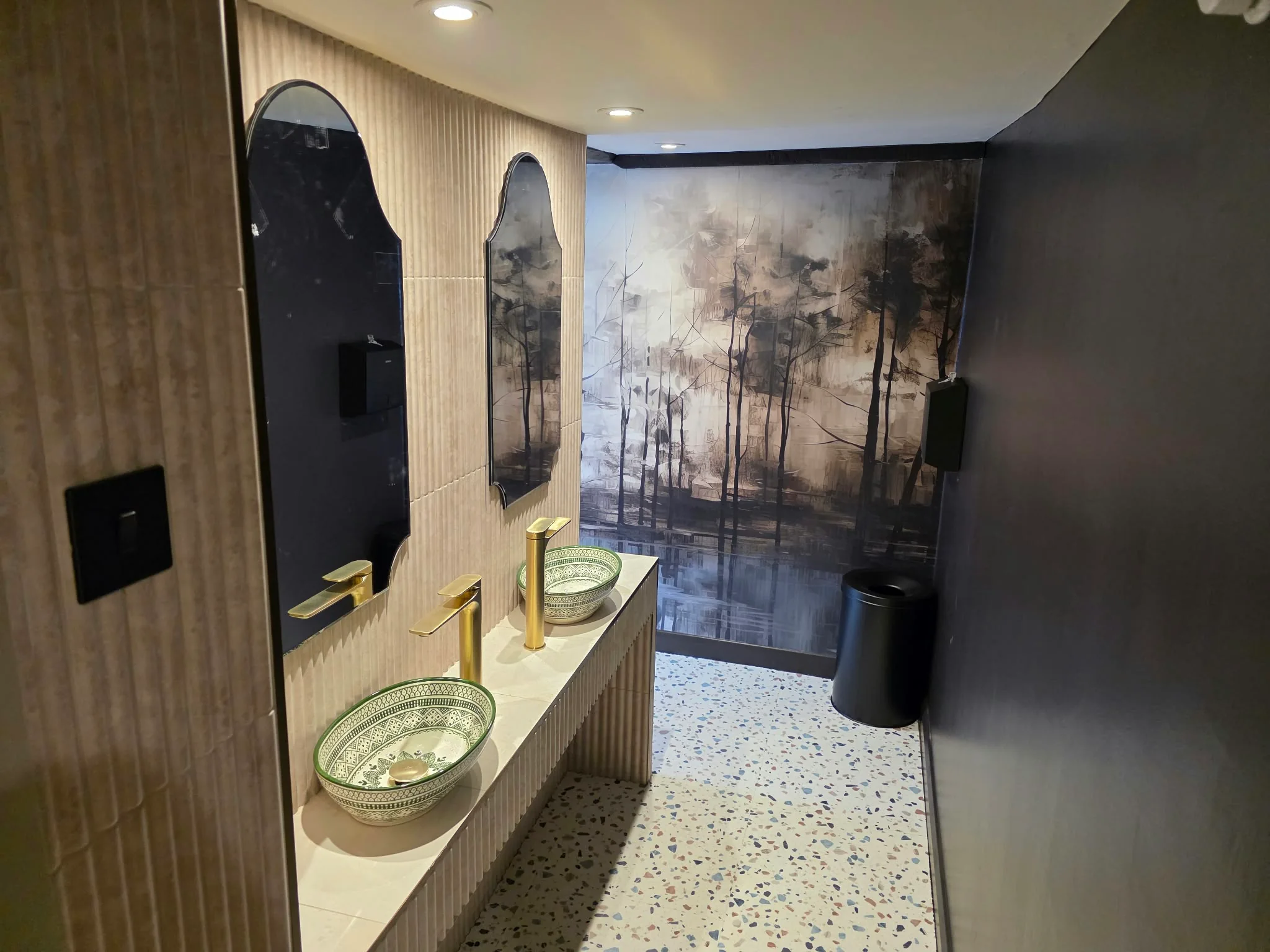 Washroom with vessel basins, fluted panelling and a forest mural