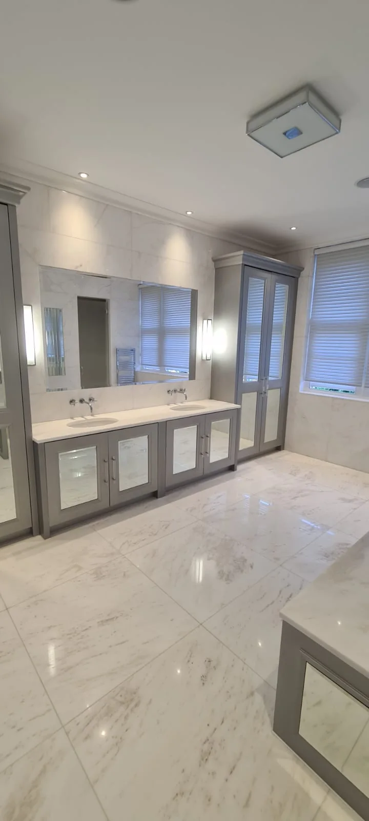 Marble bathroom with twin vanity units and mirrored cabinetry