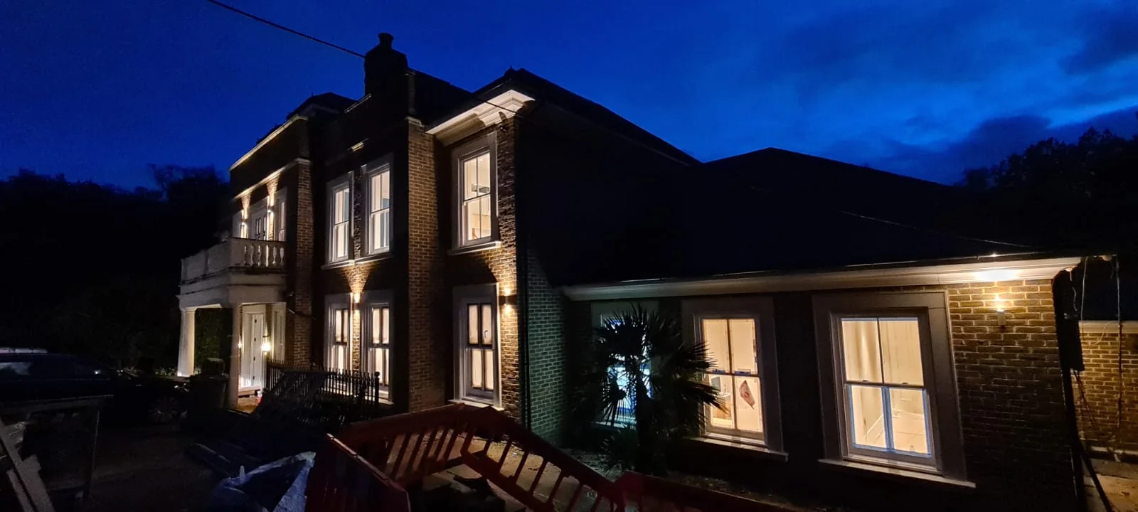 Brick country house with warmly lit sash windows at dusk, Virginia Water