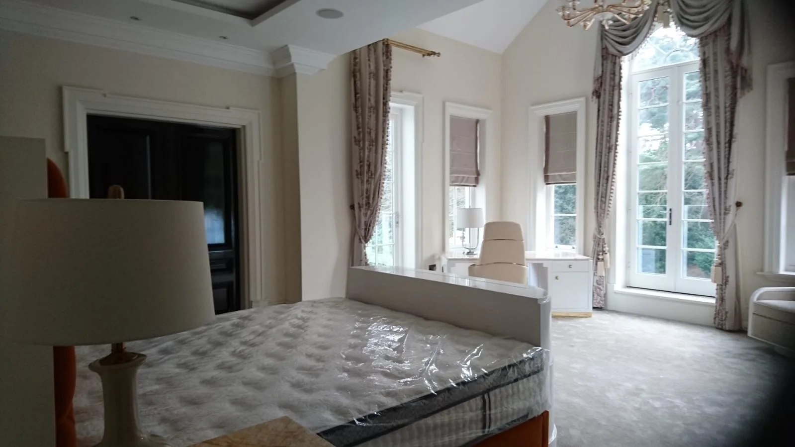Bedroom with tall arched windows, swagged curtains and a crystal chandelier