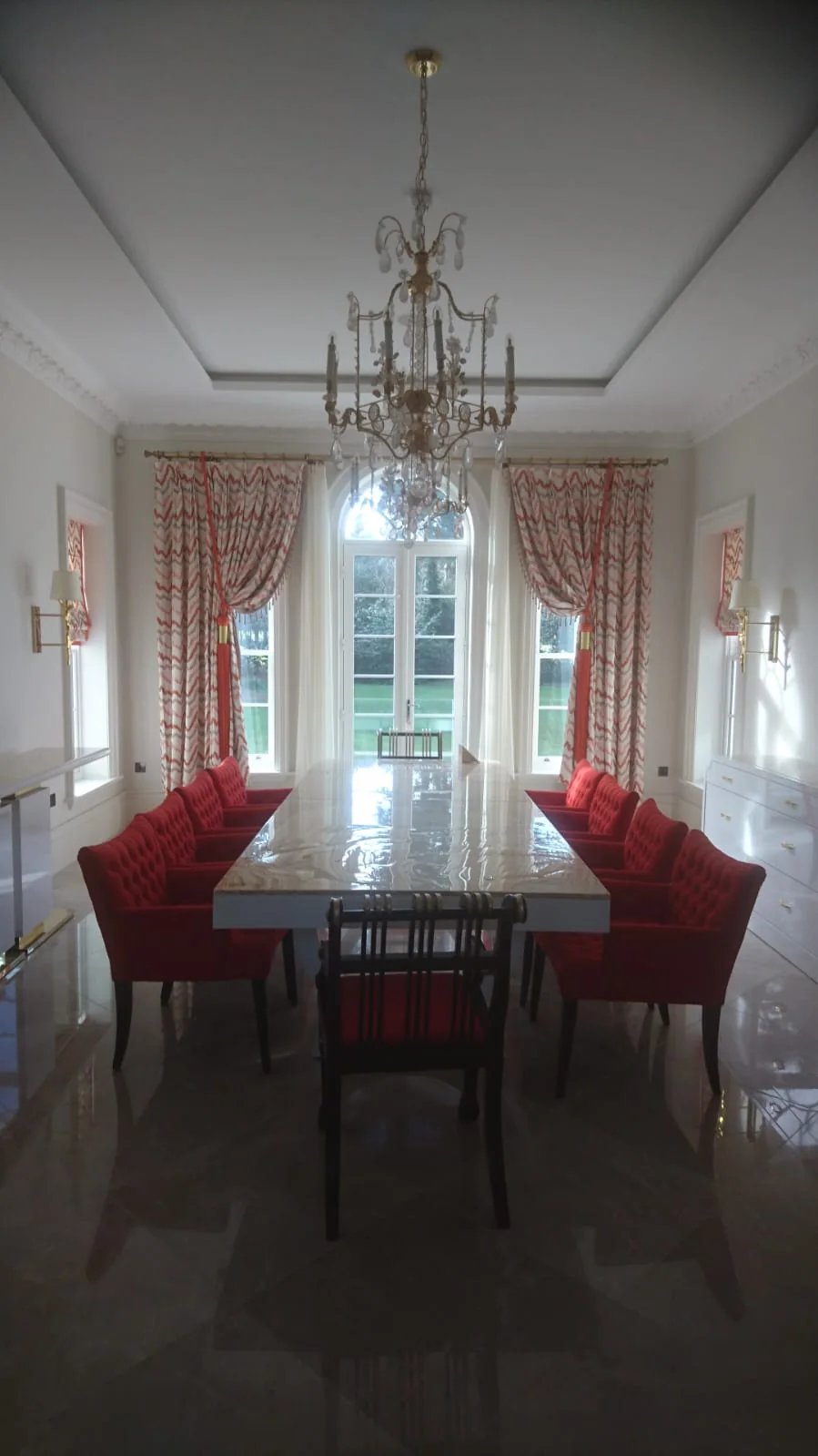Formal dining room with a marble table, red upholstered chairs and a chandelier